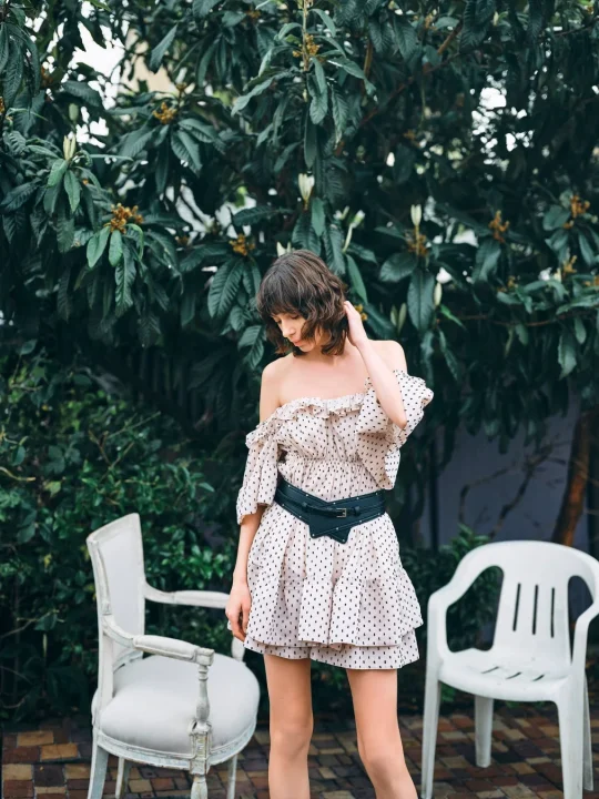 水玉模様のオフショルダーワンピースと太いベルトを着用した女性