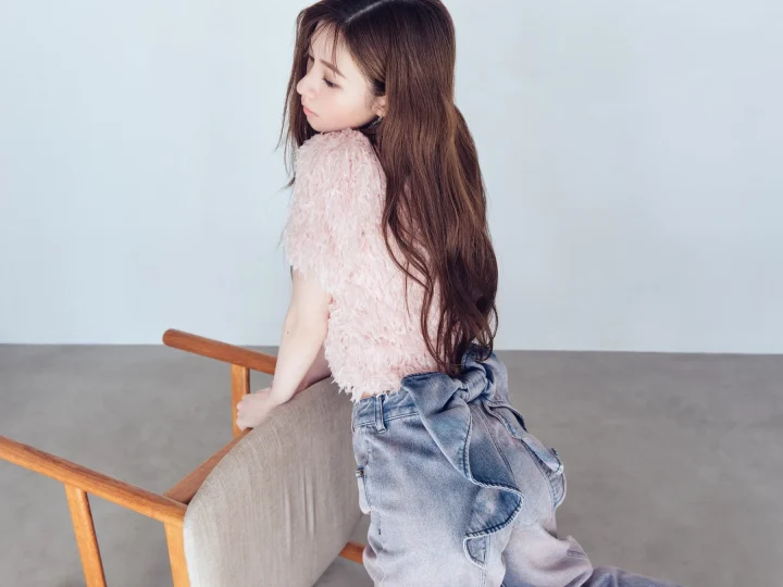 ピンクのふわふわしたトップスとデニムのサロペットを着た女性