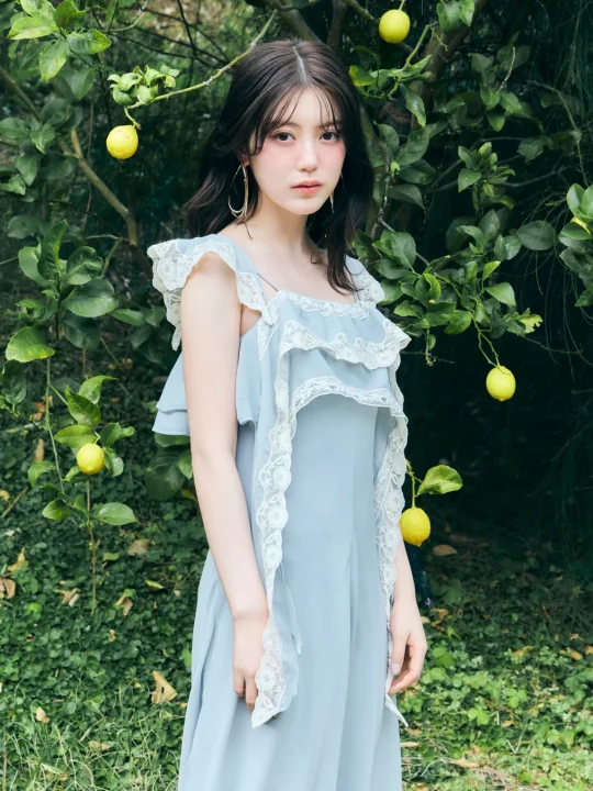 レモンが実る木の前で、水色のフリルとレースのドレスを着た若い女性