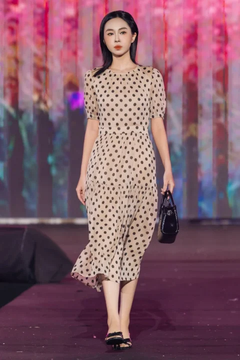 ベージュ地に黒い水玉模様のミディ丈ワンピースを着用したモデル