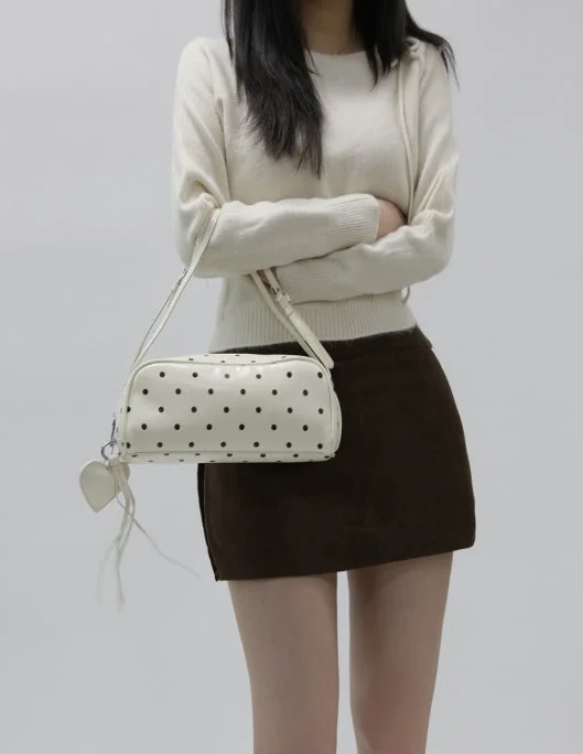 白いセーターと茶色のミニスカートを着た女性が、水玉模様の白いショルダーバッグを持っている全身ショットです。背景はシンプルな白で、カジュアルながらも洗練されたファッションスタイルを見せています。