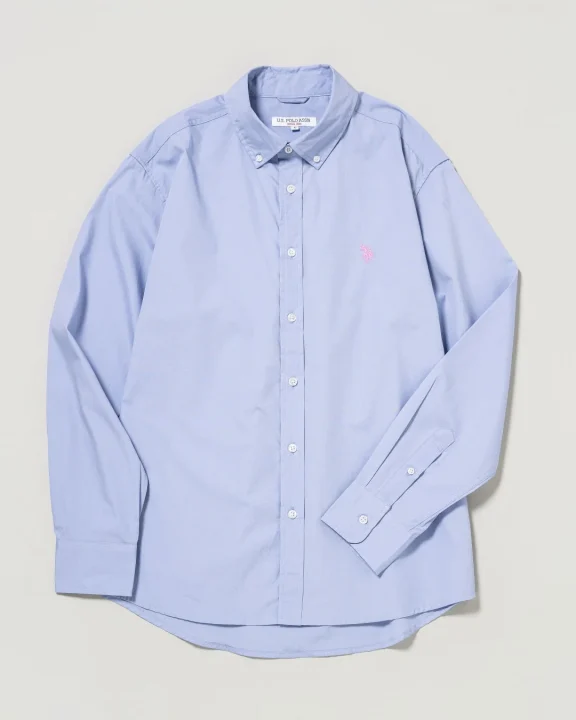 明るい水色の長袖ボタンダウンシャツが平置きされており、左胸にはピンク色のU.S. POLO ASSN.のロゴが見えます。シンプルでカジュアルなトップスです。