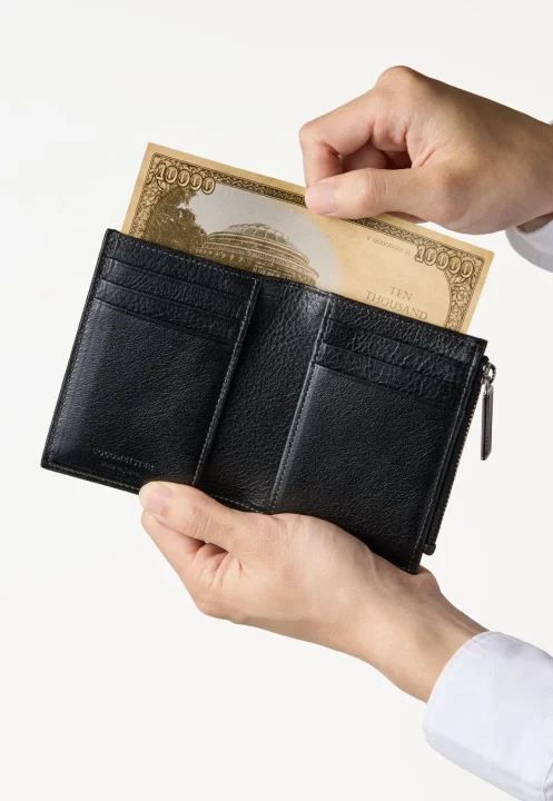 人物の手が黒い革製の二つ折り財布を持ち、1万円札を出し入れしている様子を捉えた画像です