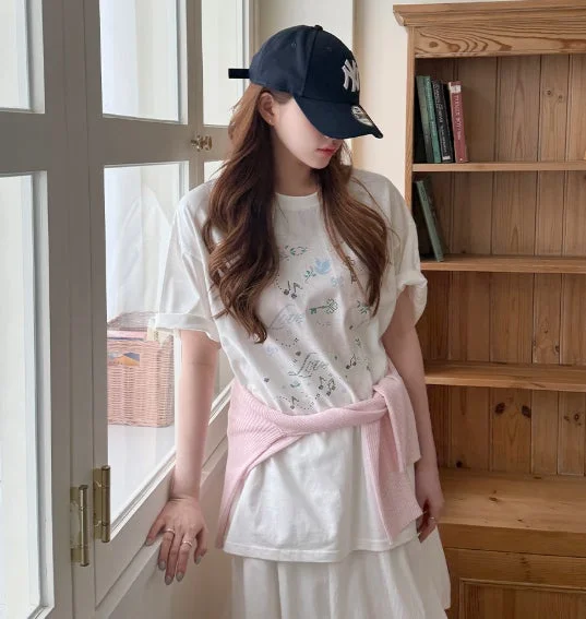 ネイビーのキャップと白いTシャツにピンクのカーディガンを巻いた女性