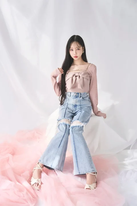 ピンクのリボントップスとダメージジーンズを着用した女性