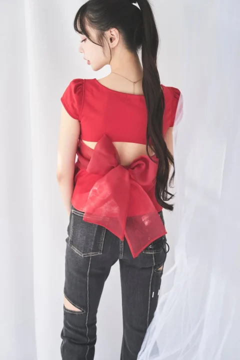 赤いトップスとリボンを背中につけた女性の後ろ姿