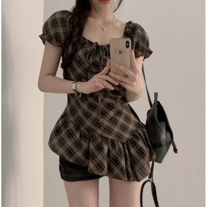 チェック柄のパフスリーブブラウスとショートパンツを着用し、スマートフォンでセルフィーを撮っている女性