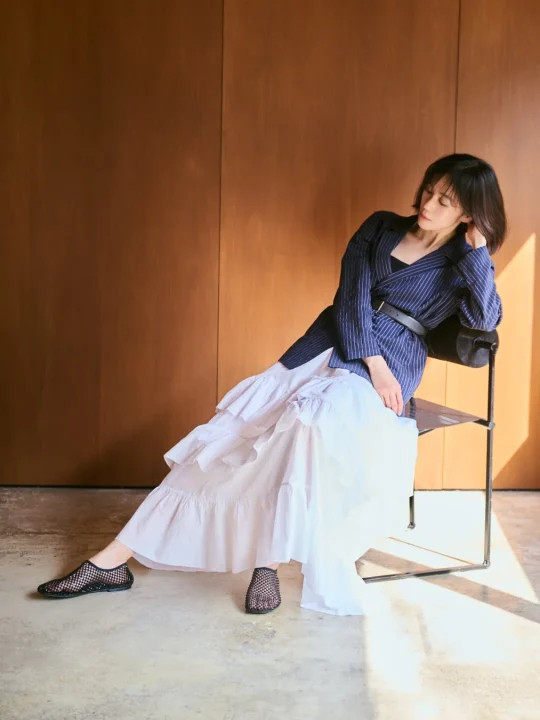 ストライプのジャケットと白いティアードスカートを着用したリラックスしたポーズ