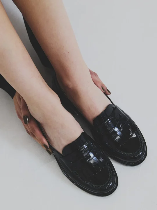 黒いフリンジ付きエナメルローファーを履いた女性の足元