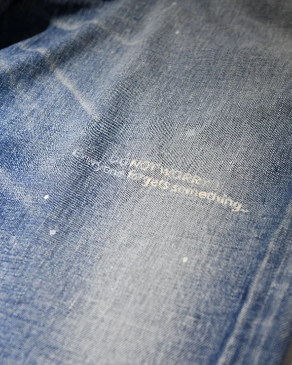 青いデニム生地のクローズアップ画像。白い文字で「DO NOT WORRY. Everyone forgets something.」というメッセージが記されています。
