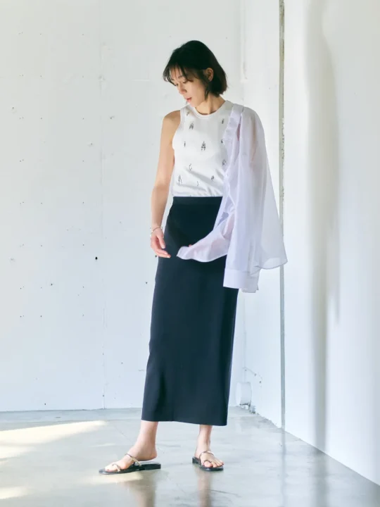 白いタンクトップと黒いロングスカートに白いシャツを肩にかけたスタイル