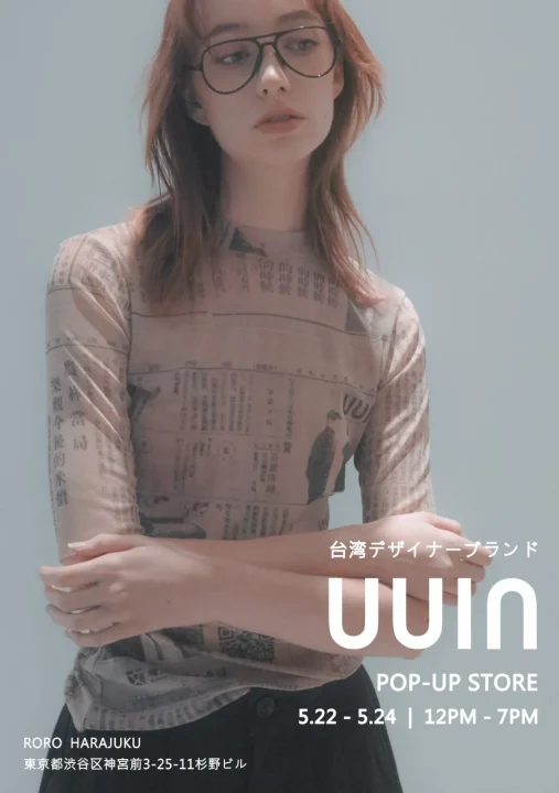 眼鏡をかけた女性が新聞記事のような柄のトップスを着用