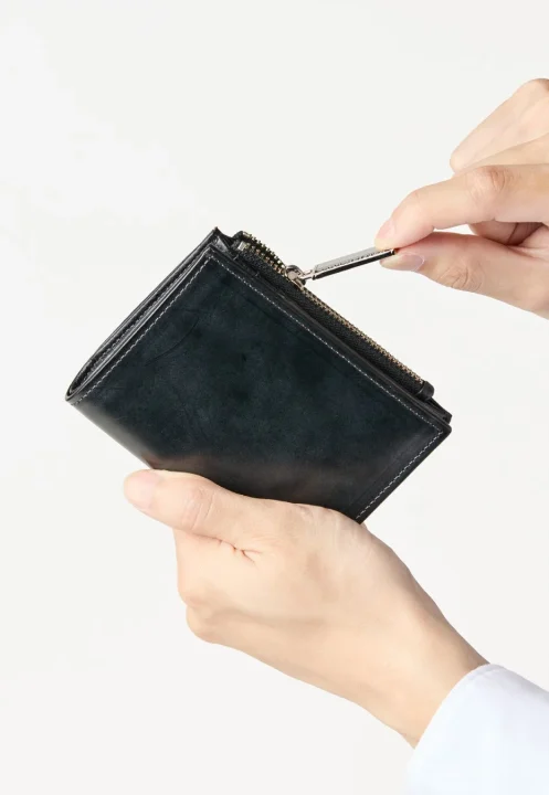 濃い色の革製財布を両手で持ち、ジッパー部分を開閉している様子を捉えた画像です