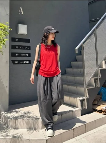 赤いノースリーブのトップスとグレーのルーズパンツを着用し、黒いキャップをかぶった女性