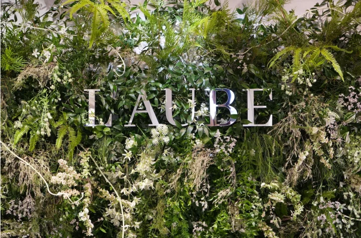 緑豊かな様々な植物と白い花で装飾された壁に、「L'AUBE」という文字が立体的に配置されています。