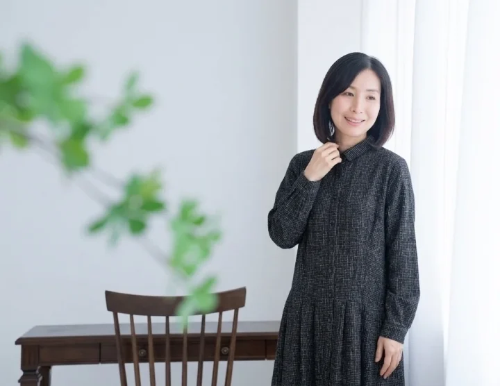 笑顔の女性がチェック柄のワンピースを着て室内に立っている