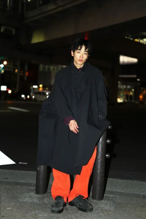 夜の都市、黒コートとオレンジパンツの男性