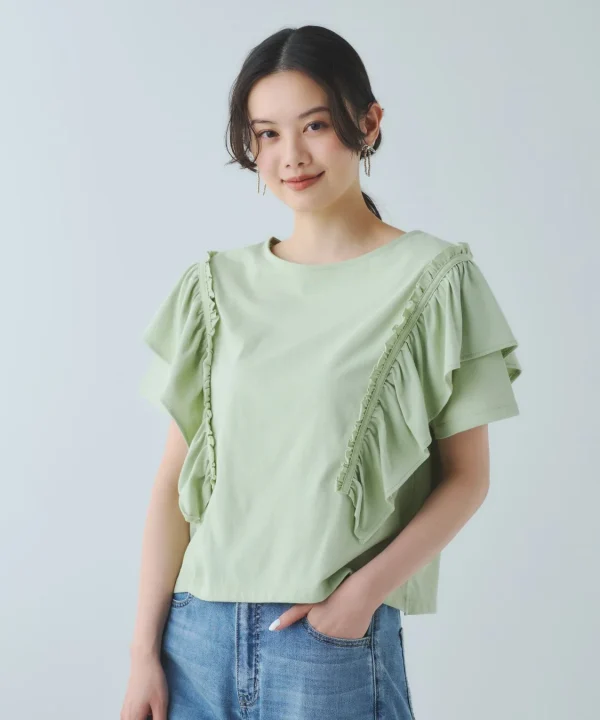 白い背景の前で、薄緑色のフリル付きトップスとデニムジーンズを着用した若い女性が、穏やかな笑顔でカメラを見つめているポートレート写真です。爽やかな印象を与えます。