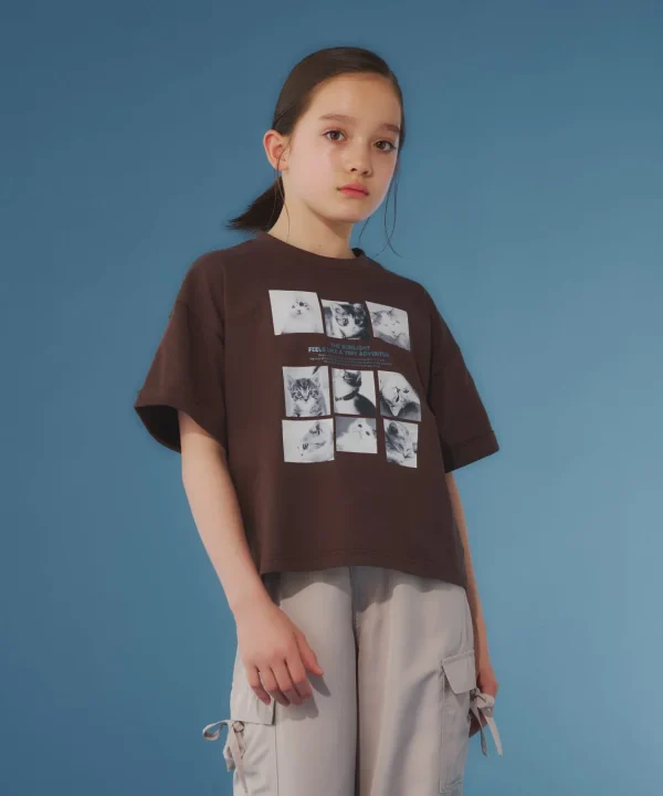 少女が、白いTシャツとピンクのショートパンツを着用し、白い背景の前でポーズをとっています。Tシャツはレースの裾飾りがあり、カジュアルながらもかわいらしいスタイルです。