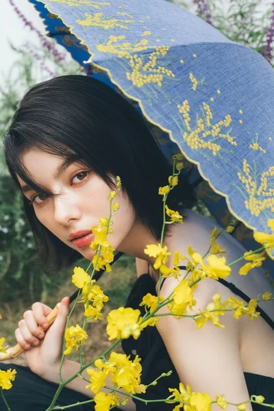青い傘と鮮やかな黄色い花に囲まれたショートヘアの女性