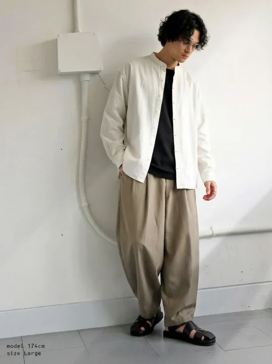 白のバンドカラーシャツに黒Tシャツ、ベージュワイドパンツを合わせた男性