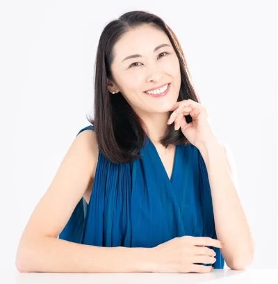 青いノースリーブの服を着たアジア人女性が、白い背景の前で明るい笑顔を見せています