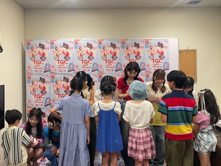 「TGC teen 2026 Summer」のポスターが貼られた屋内で、子供たちと若い女性たちが集まり、楽しそうに交流している様子が捉えられています。