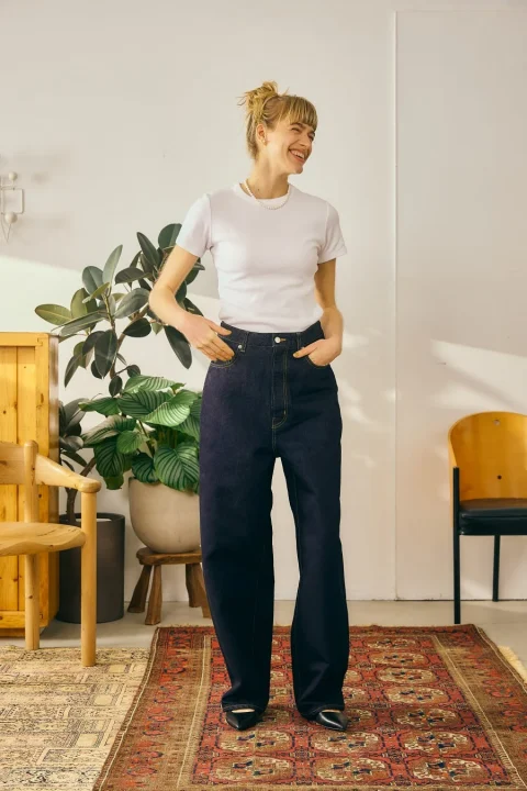 白いTシャツと濃い色のワイドレッグジーンズを着用し、パールネックレスをつけた女性