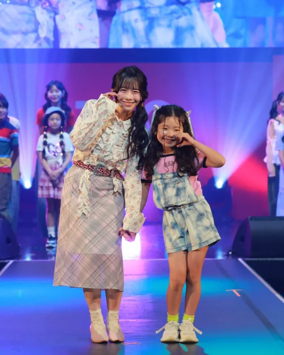 ランウェイで笑顔でポーズをとる女性と少女。