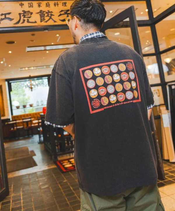 中華料理店の入り口に立つ男性の後ろ姿。男性は背中に中華風のデザインが施された黒いTシャツを着用しており、店の看板には「龍虎餃子」の文字が見える。カジュアルな雰囲気のシーン。
