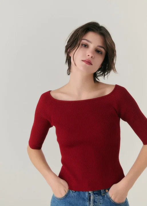 赤いボートネックリブニットとジーンズを着用した女性
