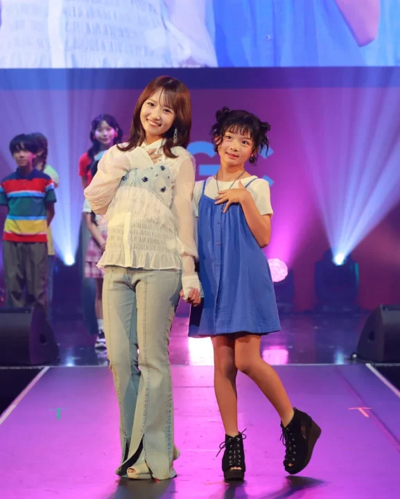 ファッションイベントのステージで、笑顔の女性と子供が並んでポーズをとっています。