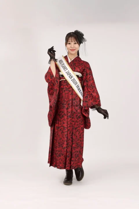 赤い着物と袴を着用し、たすきをかけたミスコンテスト出場者のような女性