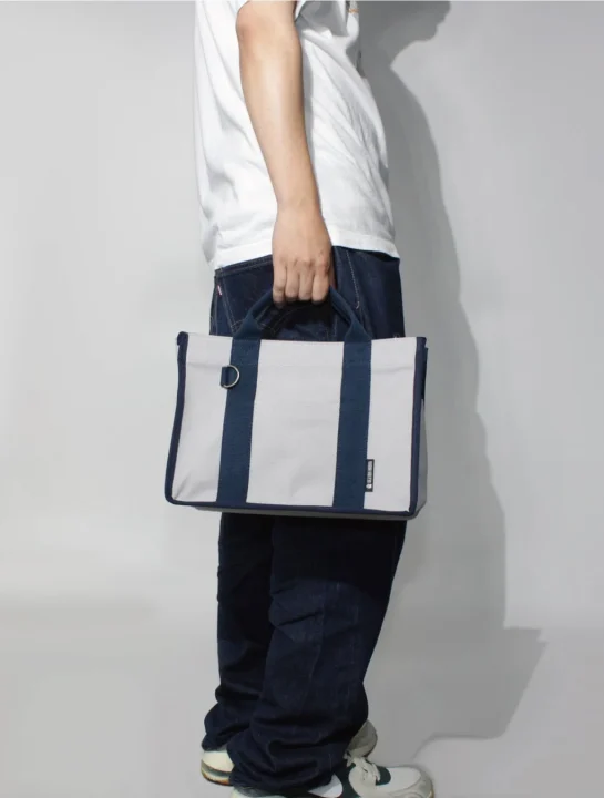 白いTシャツとジーンズを着用した人物が、ネイビーとグレーのツートンカラーのトートバッグを持っている横からの全身ショットです