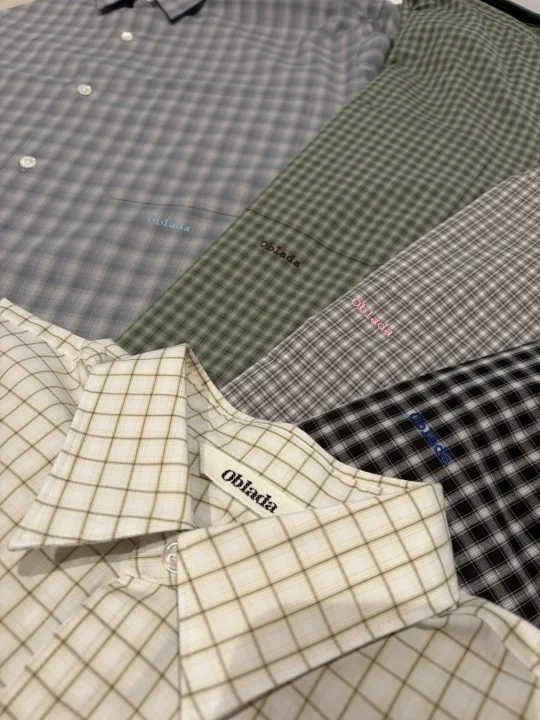 「Oblada」ブランドのチェック柄シャツが複数枚、様々な色で重ねて置かれている