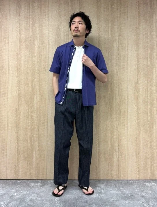 ネイビーの開襟シャツを白のヘンリーネックTシャツの上に羽織り、ダークカラーのワイドパンツと黒いサンダルを合わせる