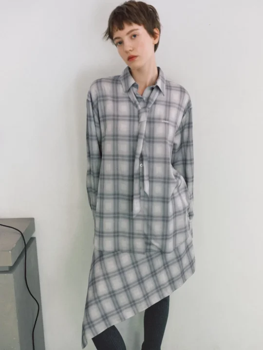 グレーのチェック柄シャツとアシンメトリーなスカートを着用したショートヘアの女性