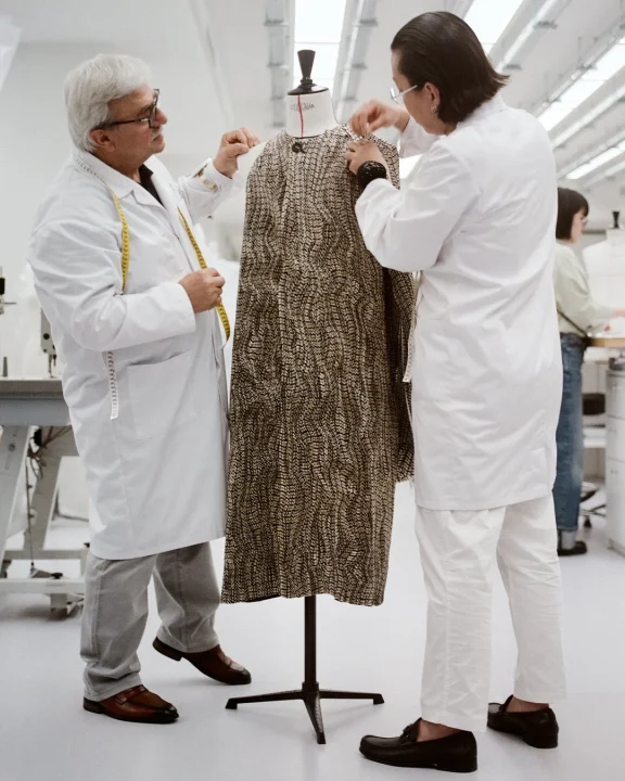 白い白衣を着た2人の職人が、マネキンにかけられた柄物の衣服を丁寧に調整している。