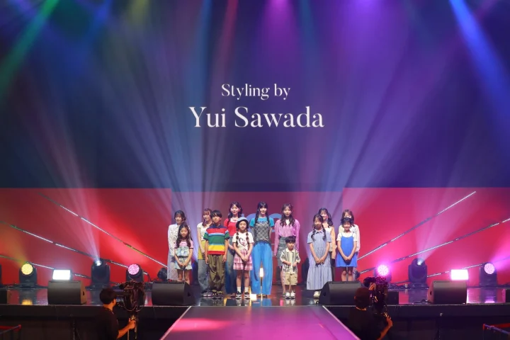 「Styling by Yui Sawada」と表示されたステージで、様々な年齢の子供や若者たちがポーズをとっています。