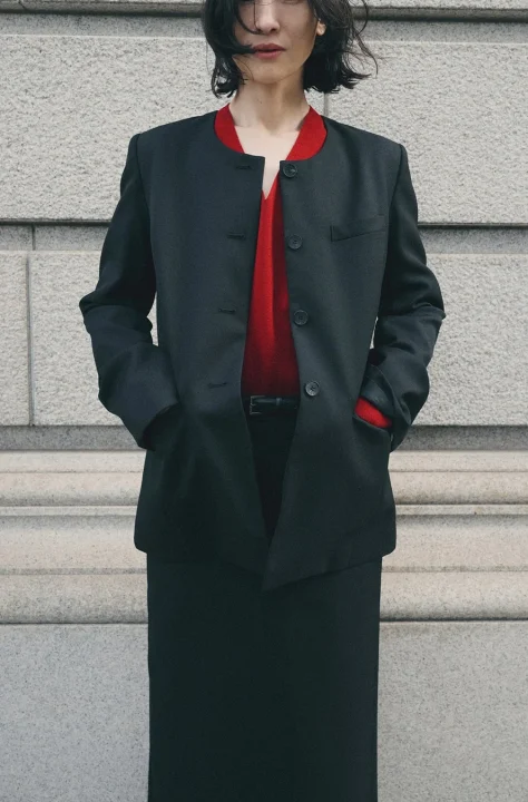 赤のトップスに黒のノーカラージャケットとスカートを着用した女性