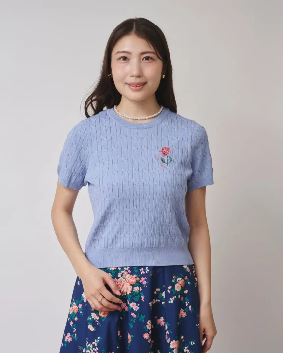 水色のケーブル編み半袖ニットとネイビーの花柄スカートを着用した若い女性