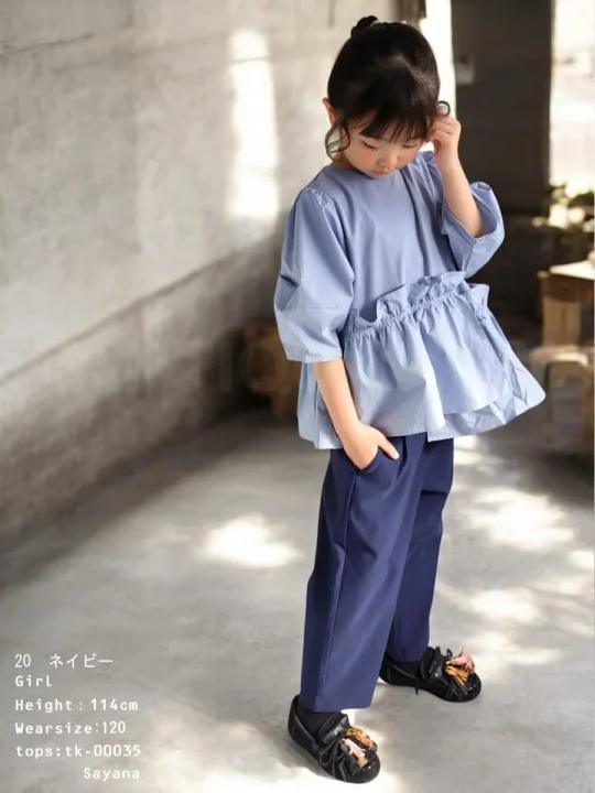 水色のフリル付きトップスとネイビーのパンツを着用した幼い女の子