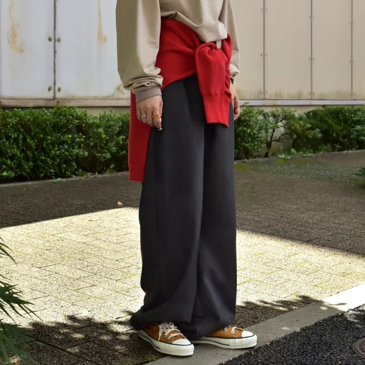 ボーダー柄のトップスに黒のワイドパンツ、腰には赤のセーターを巻いたカジュアルなコーディネート