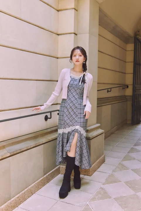 チェック柄のロングワンピースにピンクのショートカーディガンと黒い厚底ブーツを合わせた女性
