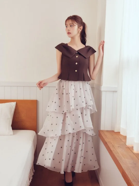 ブラウンのノースリーブトップスと白のドット柄ティアードスカートを着用した若い女性
