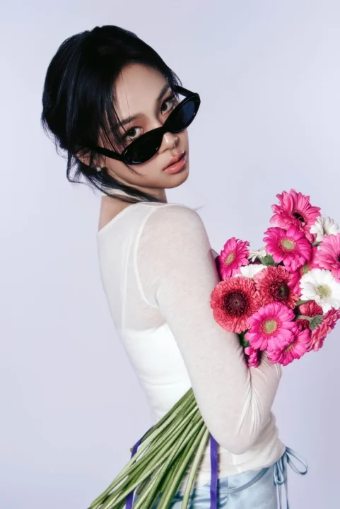 サングラスをかけ、白いトップスを着た女性が、ピンクや赤のガーベラの花束を抱え、クールな表情で振り返るポートレート。スタイリッシュで魅力的な雰囲気が漂う一枚です。