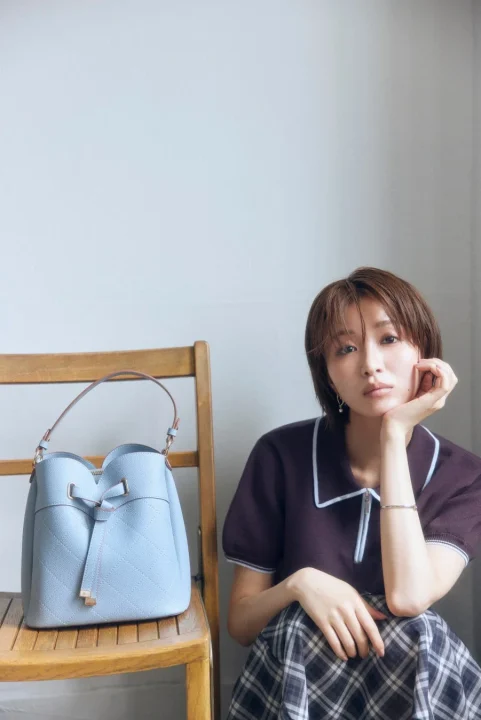 水色のバケットバッグを持つショートヘアの女性