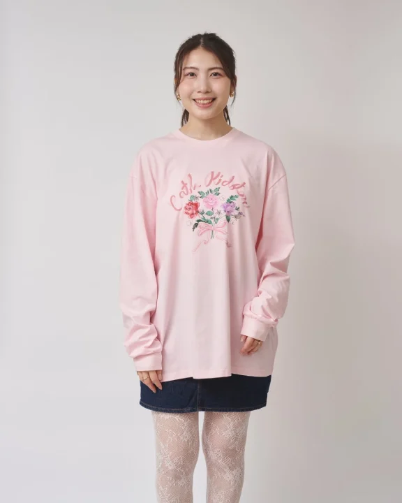 笑顔の若い日本人女性が、ピンクの長袖Tシャツ、デニムのミニスカート、白いレースタイツを着用