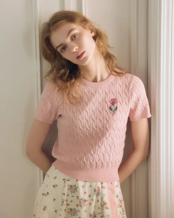 ピンクのケーブルニットトップスと花柄のスカートを着用した若い女性