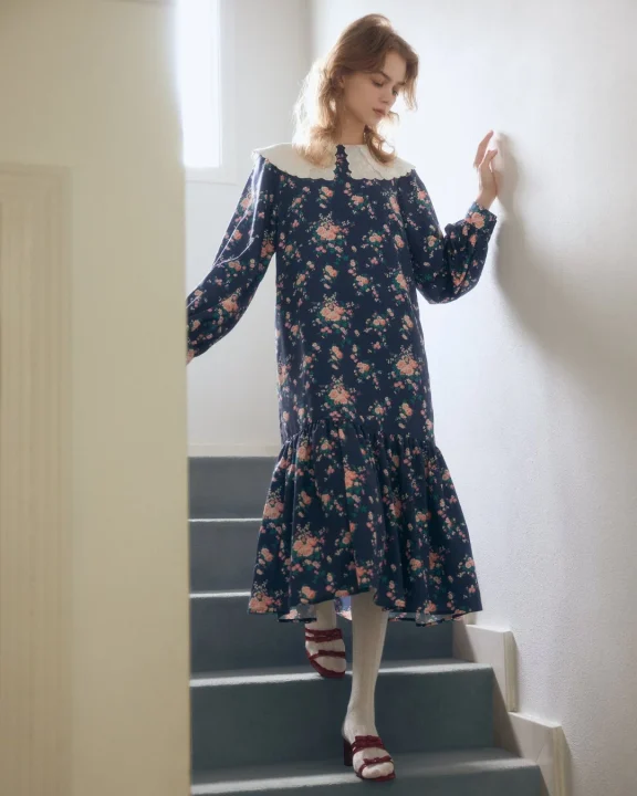 明るい室内の階段を降りる女性のポートレート。ネイビーの花柄ロングドレスと白い襟が特徴的